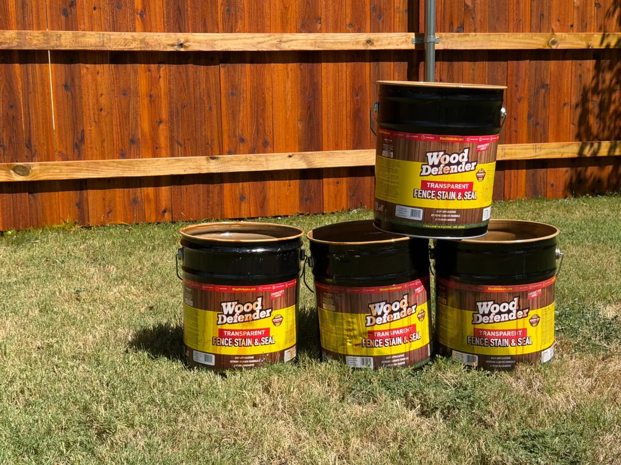 Wood Defender oil-based stain buckets in front of a Cedar Tone fence